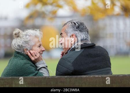 Heureux couple senior partageant des écouteurs, écoutant de la musique dans le parc Banque D'Images