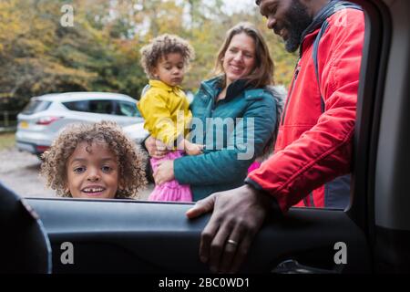 Portrait sourire garçon debout à l'extérieur de la voiture avec la famille Banque D'Images