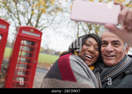 Affectueux couple senior prenant selfie dans le parc d'automne en face de l'annuaire téléphonique rouge Banque D'Images