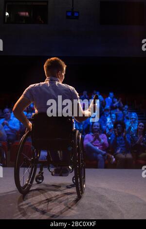 Haut-parleur femelle avec microphone en fauteuil roulant sur scène Banque D'Images