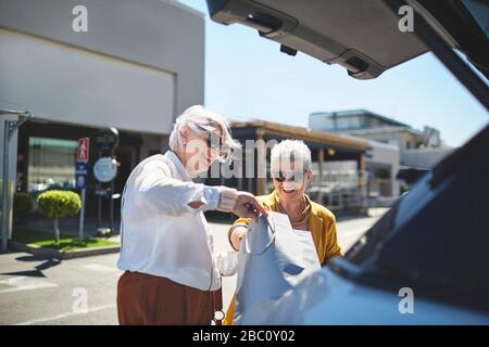 Des femmes âgées amis chargeant des sacs de shopping à l'arrière de la voiture dans le parking ensoleillé Banque D'Images