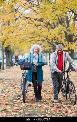 Couple senior marchant des vélos parmi les arbres et des feuilles dans le parc d'automne Banque D'Images