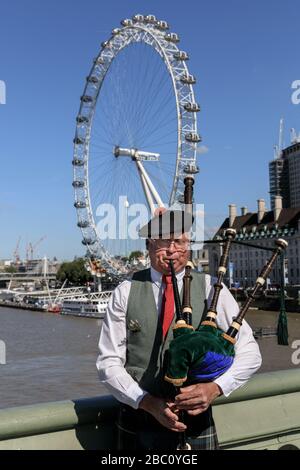 Une pipette joue des cornemuses traditionnelles sur le pont Westminster avec le London Eye en arrière-plan, Londres, Royaume-Uni Banque D'Images