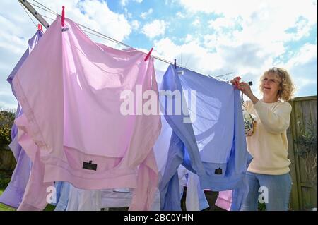 Femme accrochant différentes chemises colorées pour Homme sur une ligne de lavage rotative pendant au vent dans le jardin arrière Royaume-Uni Banque D'Images