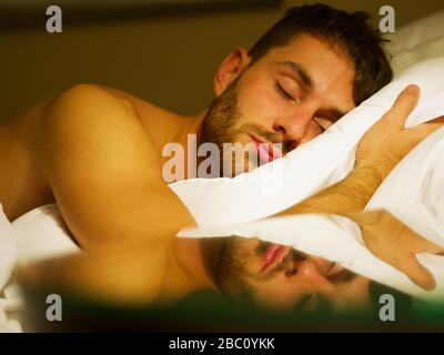 Gros plan d'un homme dormant dans un lit avec des draps blancs et réflexion sur la table de nuit. Banque D'Images