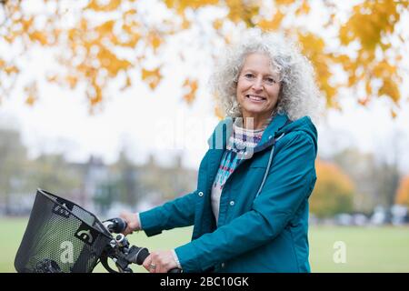 Portrait confiant, souriant femme senior vélo équitation dans le parc d'automne Banque D'Images