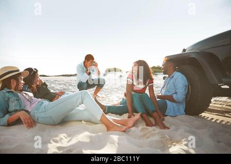 Jeune homme avec appareil photo numérique photographier des amis accrochés sur la plage ensoleillée Banque D'Images