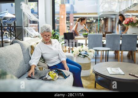 Femme senior regardant les nuances de tissu sur le canapé dans la boutique de décoration de maison Banque D'Images