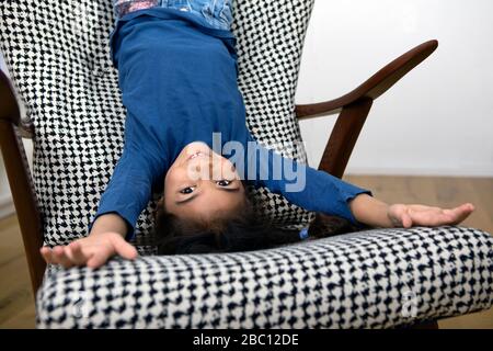 Portrait de la petite fille penchée à l'envers du dossier d'un fauteuil Banque D'Images