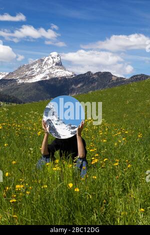 Femme assise dans un pré, se cachant derrière le miroir, reflétant les montagnes de Val Badia, Alto Adige, Italie Banque D'Images