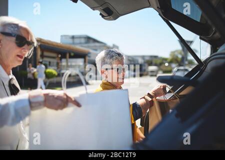 Les femmes âgées chargent des sacs de shopping à l'arrière de la voiture dans le parking ensoleillé Banque D'Images