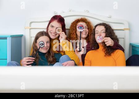 Portrait de famille de la mère et de ses trois filles assis ensemble sur un lit tenant des masques en papier Banque D'Images