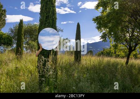 Femme cachant l'arbre de behing, tenant miroir, reflétant le ciel Banque D'Images