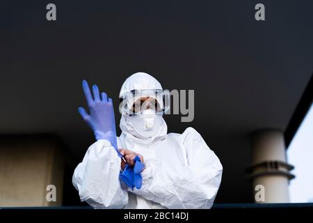 Femme scientifique portant un costume et un masque de protection et mettant des gants de protection Banque D'Images