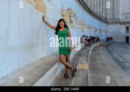 Une fille souriante dans une robe verte se tient sur les marches en marbre du monument Vittorio Emanuele II à Rome, Italie Banque D'Images