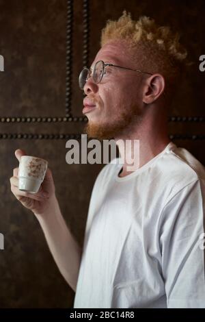Vue latérale de l'albinos homme avec des verres, ayant un café dans une cafétéria Banque D'Images