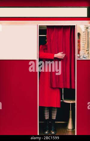 Femme portant un manteau rouge et des bottes derrière le rideau dans une cabine photo Banque D'Images