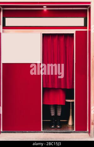 Femme portant un manteau rouge et des bottes derrière le rideau dans une cabine photo Banque D'Images