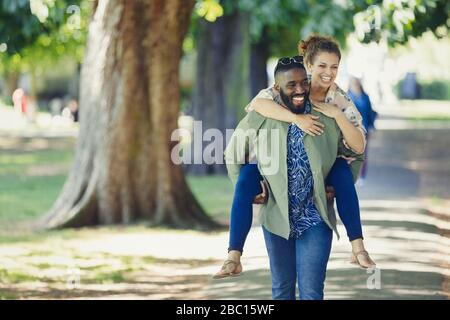 Un jeune couple amusant en porgybacking dans le parc Banque D'Images