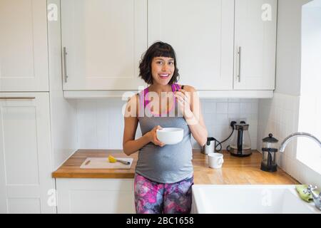 Portrait heureuse femme enceinte manger dans la cuisine Banque D'Images