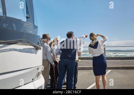 Guide touristique et touristes actifs de haut niveau regardant l'océan à l'extérieur du bus touristique Banque D'Images