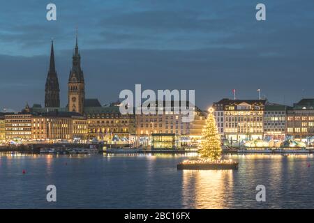 Allemagne, Hambourg, illuminé l'arbre d'Alstertanne au crépuscule avec la promenade de Jungfernstieg et l'église Saint-Nicolas en arrière-plan Banque D'Images