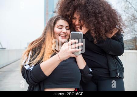 Deux jeunes femmes sportives heureuses utilisant un smartphone dans la ville Banque D'Images