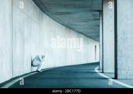 Homme déapparié portant des vêtements de protection penchant contre le mur de béton dans un tunnel Banque D'Images