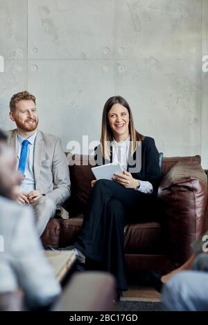 Un homme d'affaires et une femme d'affaires heureux assis sur un canapé dans le hall de l'hôtel pendant une réunion Banque D'Images