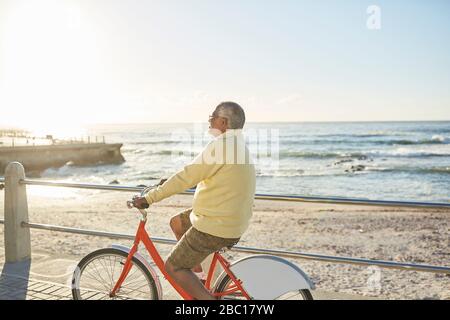 Active homme senior à vélo touristique sur promenade ensoleillée le long de l'océan Banque D'Images