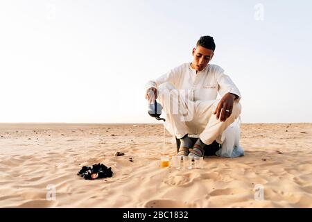 Homme qui verse du thé dans des glasss dans le désert du Sahara, Tindouf, Algérie Banque D'Images