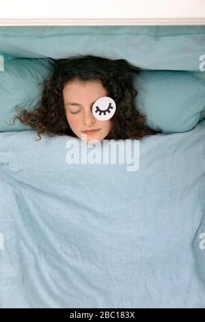 Portrait de la jeune femme endormie posée dans le lit avec masque en papier Banque D'Images