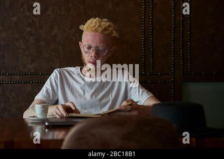 Albino homme ayant un café et lire un livre dans une cafétéria Banque D'Images
