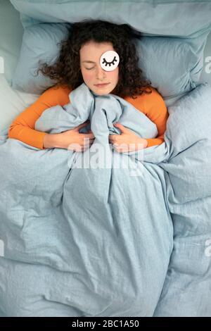 Portrait de la jeune femme endormie posée dans le lit avec masque en papier Banque D'Images