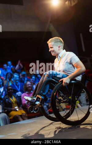 Haut-parleur féminin souriant faisant une roue en fauteuil roulant sur scène Banque D'Images