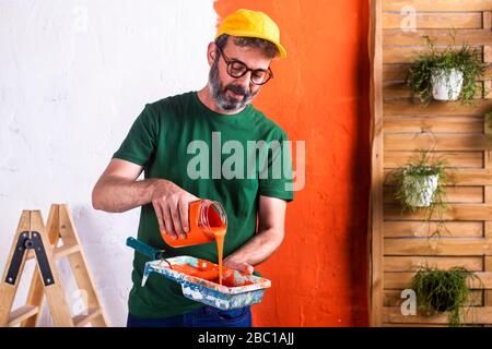 Homme qui verse de la peinture orange dans le bac à peinture Banque D'Images