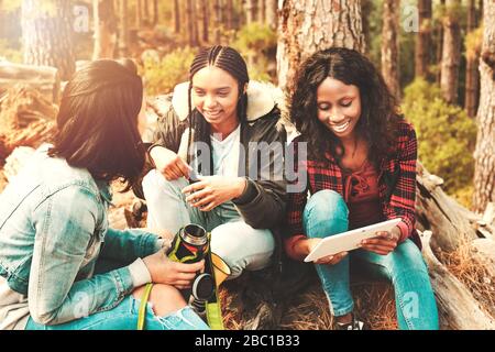 Les jeunes femmes amis boivent du café et utilisent une tablette numérique dans le bois Banque D'Images