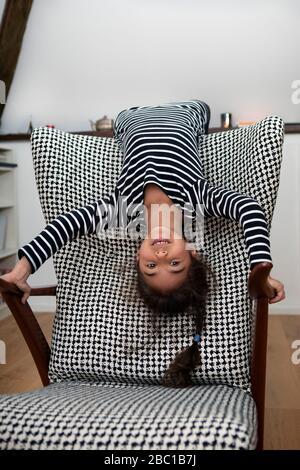 Portrait de la petite fille penchée à l'envers du dossier d'un fauteuil Banque D'Images