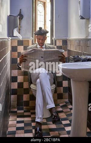 Un jeune homme d'affaires élégant avec un béret lisant le journal assis dans les toilettes Banque D'Images