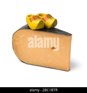 Morceau de fromage Gouda hollandais mûr avec des chaussures en bois miniatures isolées sur fond blanc Banque D'Images