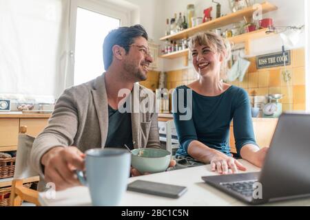 Un couple heureux assis à la table dans la cuisine avec un ordinateur portable Banque D'Images