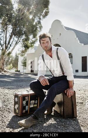 Homme dans des vêtements à l'ancienne assis sur la valise dans la campagne Banque D'Images