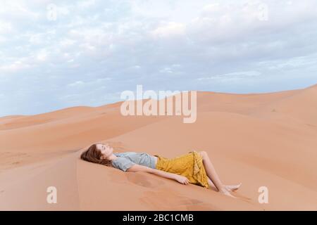 Jeune femme allongé dans une dune de sable dans le désert du Sahara, Merzouga, Maroc Banque D'Images