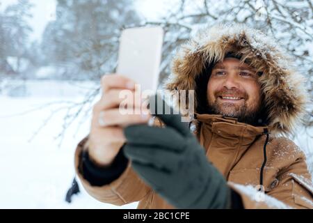 Portrait de l'homme souriant prenant selfie avec téléphone portable en hiver Banque D'Images