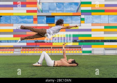 Danseuse sautant le style super héros sur partenaire, couché sur herbe Banque D'Images