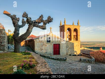 Vue sur la façade principale de l'Igreja Matriz de Castelo Rodrigo, au Portugal, et la place de l'Eglise, en hiver après une journée ensoleillée. Banque D'Images