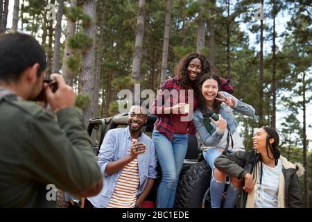 Jeune homme avec appareil photo numérique photographier des amis à la jeep dans les bois Banque D'Images