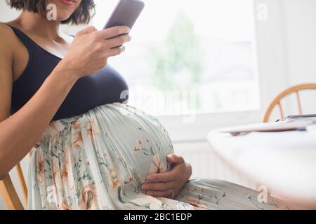 Femme enceinte en robe fleurie utilisant un smartphone Banque D'Images