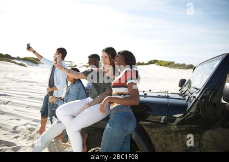 Jeunes amis avec des téléphones de caméra prenant selfie à jeep sur la plage ensoleillée Banque D'Images