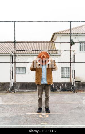 Homme debout sur un terrain de sport couvrant son visage avec un chapeau Banque D'Images